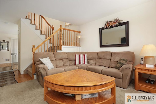 living area with stairway, visible vents, and light colored carpet