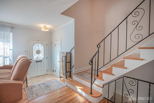 foyer featuring baseboards, wood finished floors, stairs, and crown molding