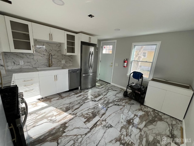 kitchen with marble finish floor, stainless steel appliances, light countertops, glass insert cabinets, and a sink