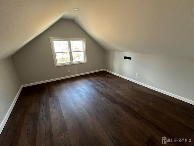 additional living space featuring dark wood-style floors, lofted ceiling, and baseboards