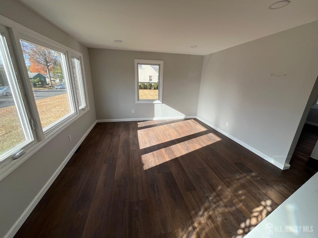 empty room with plenty of natural light, baseboards, and dark wood finished floors