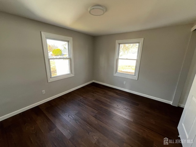 spare room with plenty of natural light, baseboards, and dark wood-type flooring