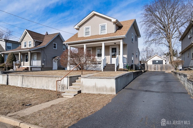 view of front of house featuring a porch, fence, a shingled roof, and aphalt driveway