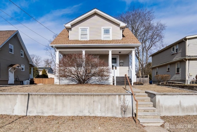 view of front of property featuring covered porch, a shingled roof, and fence