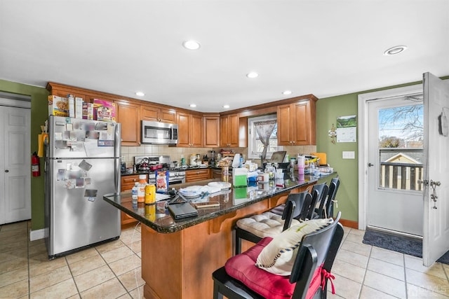 kitchen featuring stainless steel appliances, a breakfast bar area, light tile patterned floors, and dark stone counters