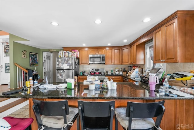 kitchen with light tile patterned flooring, appliances with stainless steel finishes, backsplash, dark stone counters, and kitchen peninsula