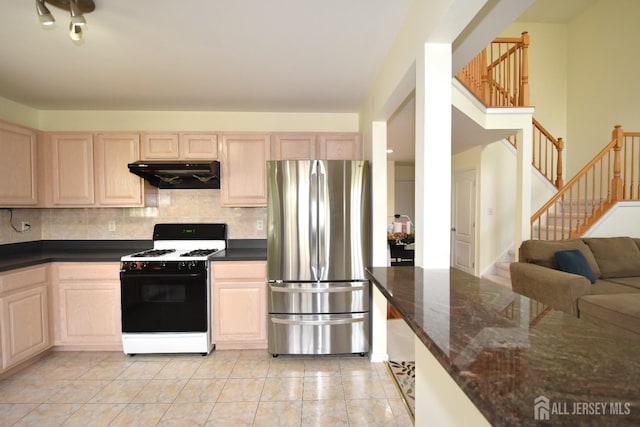 kitchen with decorative backsplash, stainless steel fridge, dark stone countertops, light tile patterned flooring, and white range with gas stovetop