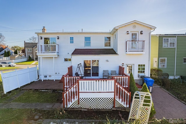 rear view of property with a balcony, fence, and a chimney