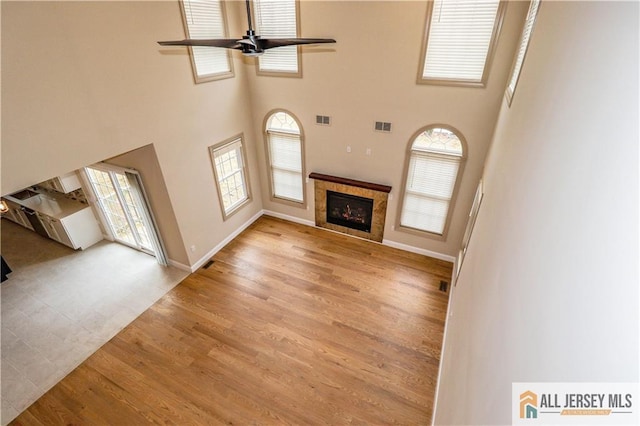 4 Kristina Ct, East Brunswick, NJ 08816 - unfurnished living room with ceiling fan, a tiled fireplace, wood finished floors, a towering ceiling, and baseboards