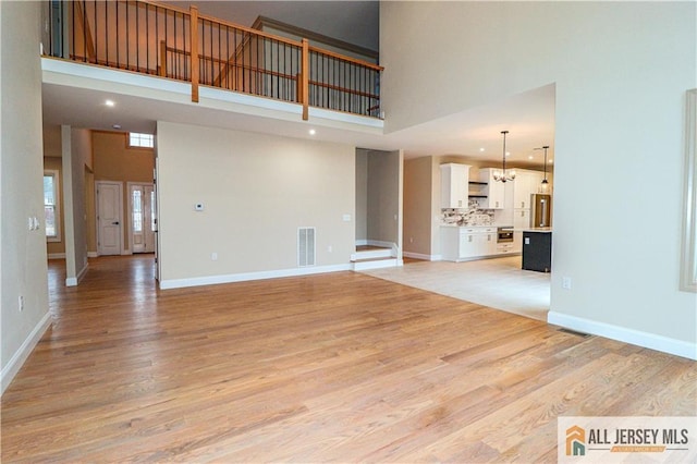 4 Kristina Ct, East Brunswick, NJ 08816 - unfurnished living room with a high ceiling, light wood-type flooring, recessed lighting, baseboards, and a chandelier