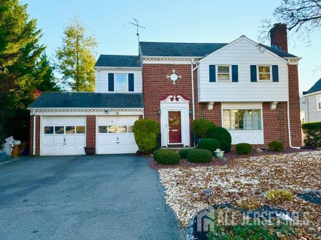 view of front of home featuring driveway, a chimney, and brick siding