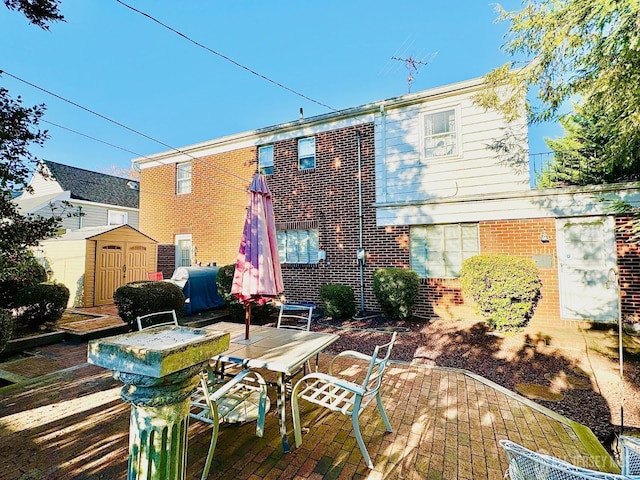 back of property with an outbuilding, a patio, brick siding, a shed, and outdoor dining space