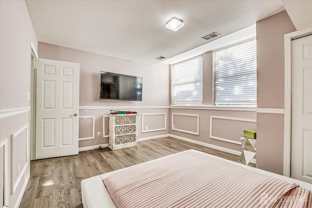 bedroom with a decorative wall, wood finished floors, and visible vents