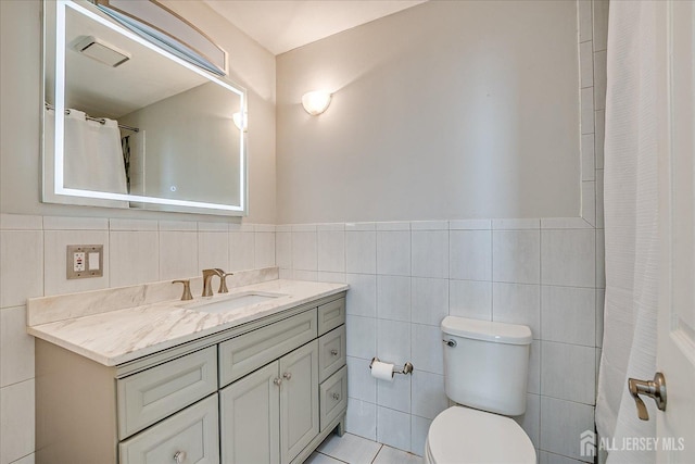bathroom with toilet, tile walls, wainscoting, visible vents, and vanity