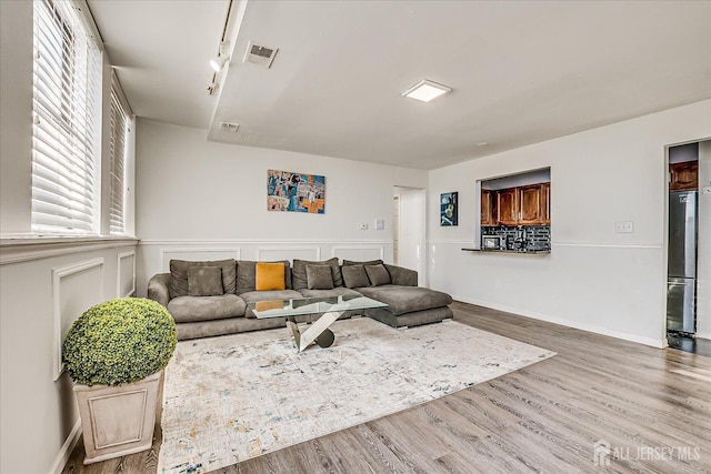 living area featuring wood finished floors, rail lighting, wainscoting, and visible vents