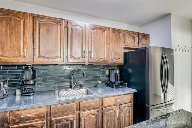 kitchen featuring dark countertops, brown cabinetry, a sink, freestanding refrigerator, and tasteful backsplash