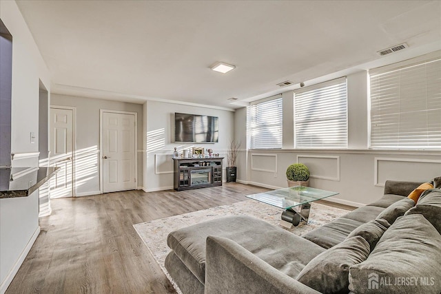 living room with baseboards, a glass covered fireplace, visible vents, and light wood-style flooring