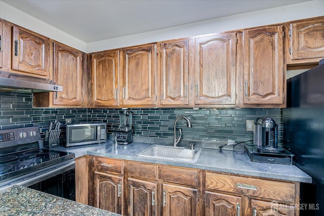kitchen with a sink, stainless steel range with electric cooktop, freestanding refrigerator, backsplash, and under cabinet range hood