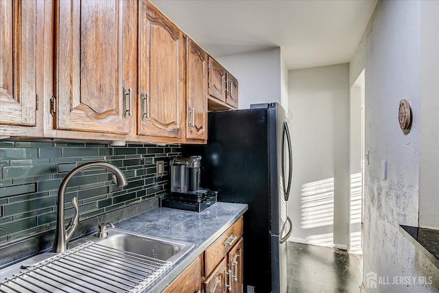kitchen featuring brown cabinetry, tasteful backsplash, a sink, and freestanding refrigerator