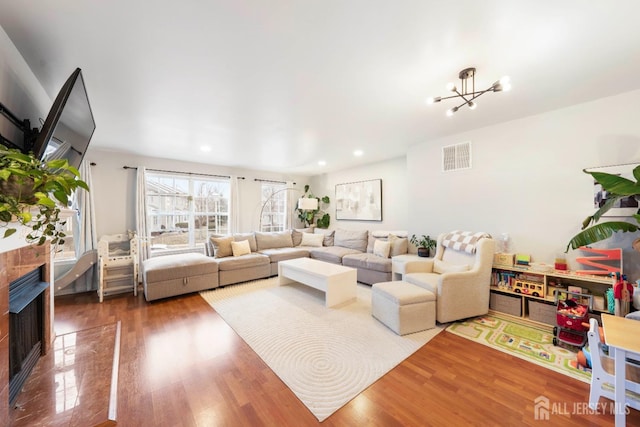 living room featuring a chandelier, wood finished floors, visible vents, and a high end fireplace