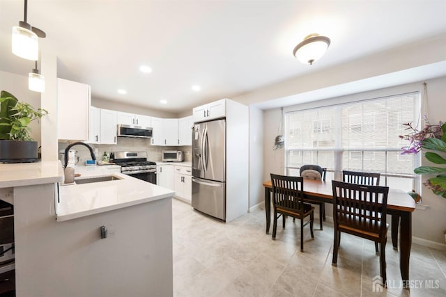 kitchen featuring tasteful backsplash, white cabinets, stainless steel appliances, light countertops, and a sink