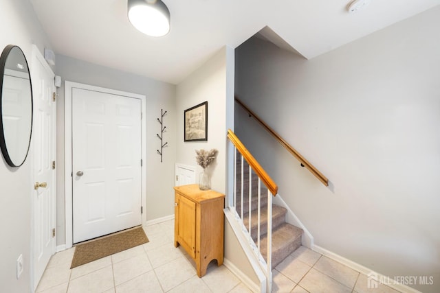 foyer featuring light tile patterned flooring, stairway, and baseboards