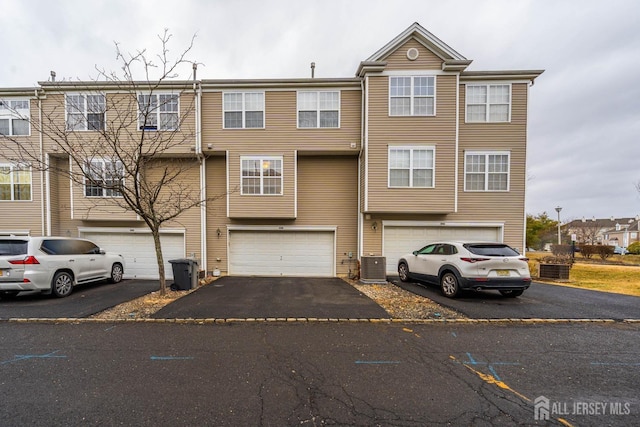 view of property with driveway, an attached garage, and central AC unit