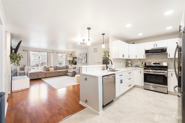 kitchen with stainless steel appliances, a peninsula, a sink, open floor plan, and backsplash