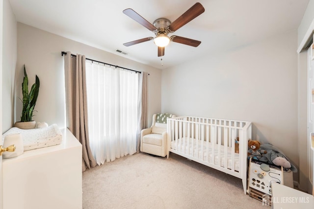 bedroom featuring a nursery area, visible vents, ceiling fan, and carpet flooring