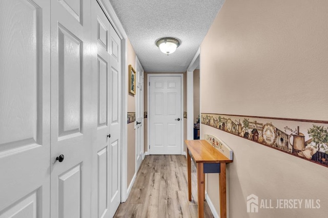 hallway featuring a textured ceiling, light wood finished floors, and baseboards