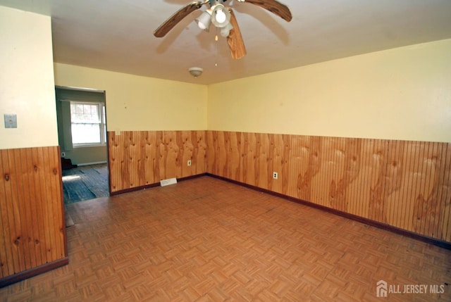 empty room with ceiling fan, dark parquet flooring, and wooden walls