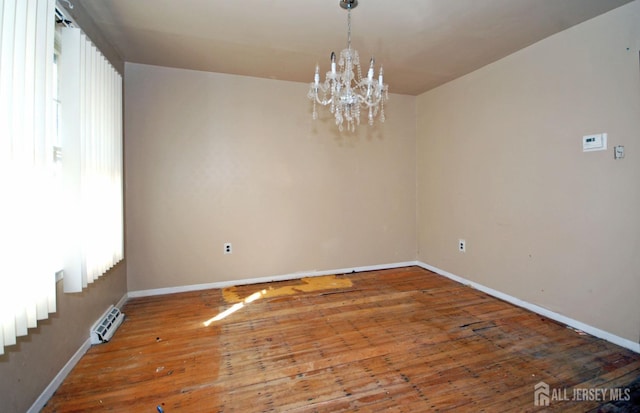 spare room featuring a healthy amount of sunlight, wood-type flooring, and an inviting chandelier