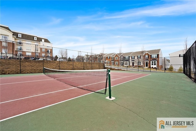 view of tennis court featuring community basketball court, fence, and a residential view