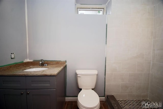 bathroom with vanity, tiled shower, toilet, and hardwood / wood-style floors