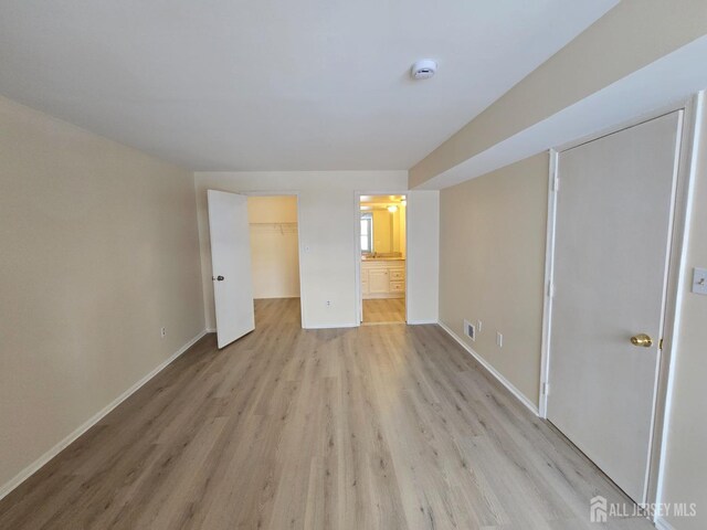 unfurnished bedroom featuring connected bathroom, a spacious closet, and light hardwood / wood-style flooring