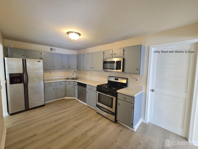 kitchen with light wood-type flooring, appliances with stainless steel finishes, sink, and gray cabinetry