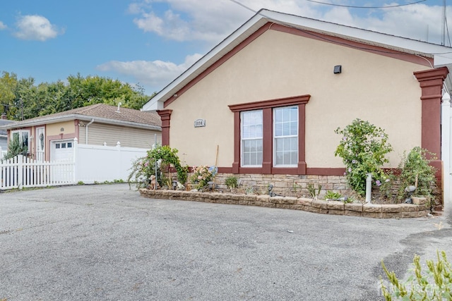 view of property exterior featuring stucco siding, driveway, a garage, and fence