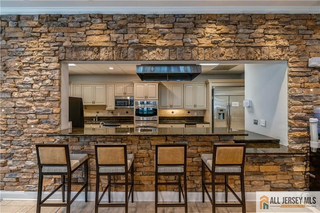 kitchen featuring a breakfast bar, dark stone counters, kitchen peninsula, stainless steel appliances, and cream cabinetry