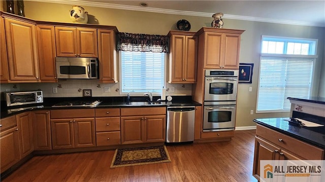 kitchen with a toaster, crown molding, dark countertops, appliances with stainless steel finishes, and a sink