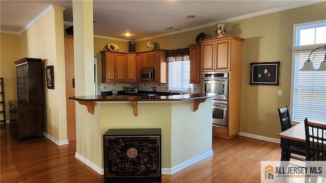 kitchen featuring crown molding, a breakfast bar area, stainless steel appliances, light wood-style floors, and baseboards