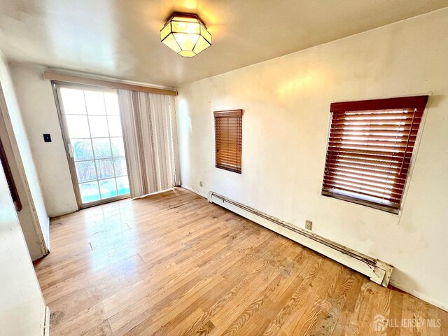 unfurnished room featuring a baseboard heating unit and wood finished floors