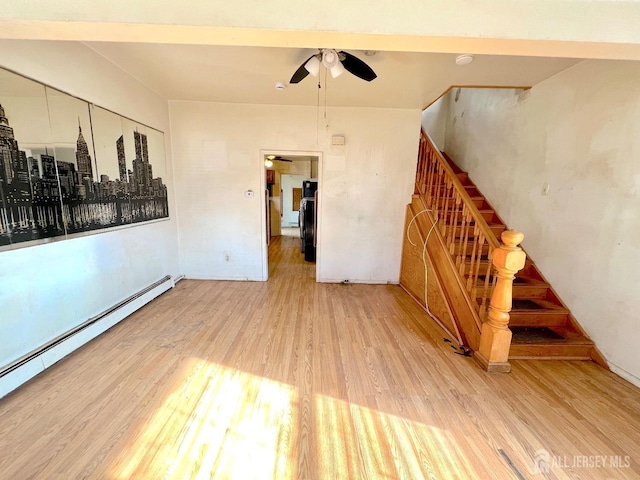 spare room featuring light wood-style floors, baseboard heating, ceiling fan, and stairs