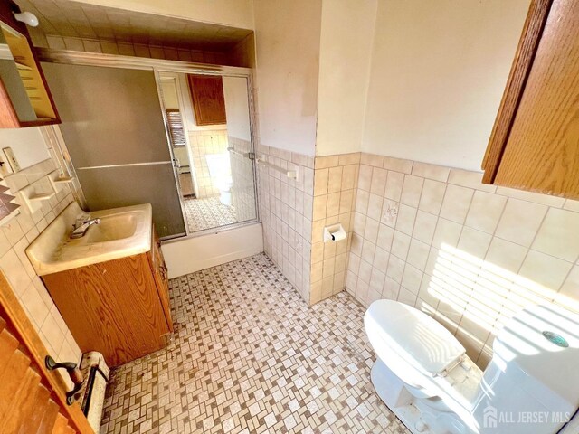 full bath with a wainscoted wall, toilet, combined bath / shower with glass door, tile walls, and vanity