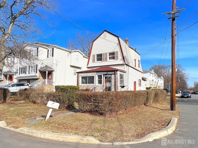 view of front facade featuring a residential view, a gambrel roof, and a chimney