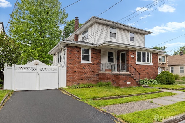 view of front of house featuring a chimney, brick siding, a gate, fence, and driveway