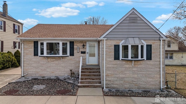 view of front facade with stone siding, a shingled roof, and fence