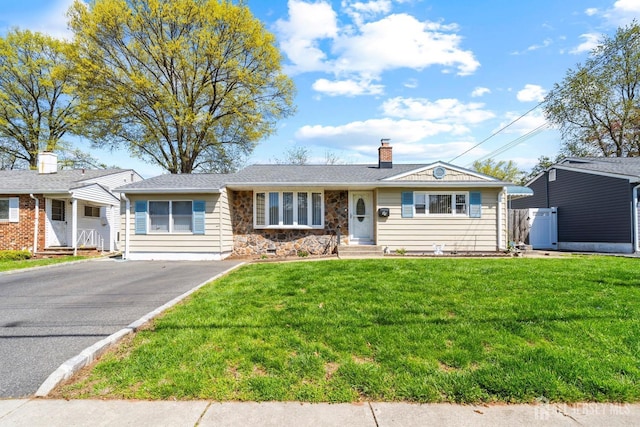single story home featuring a chimney, stone siding, asphalt driveway, and a front yard