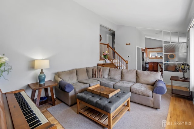 living area with light wood-style flooring, stairs, and vaulted ceiling