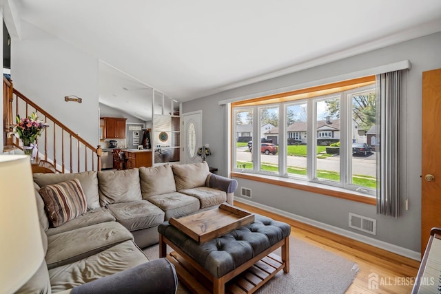 living room featuring healthy amount of natural light, light wood-style floors, stairs, baseboards, and lofted ceiling