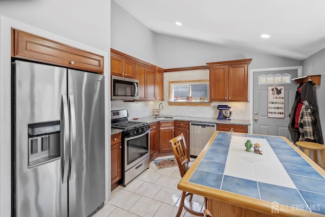 kitchen featuring appliances with stainless steel finishes, vaulted ceiling, a sink, backsplash, and brown cabinets